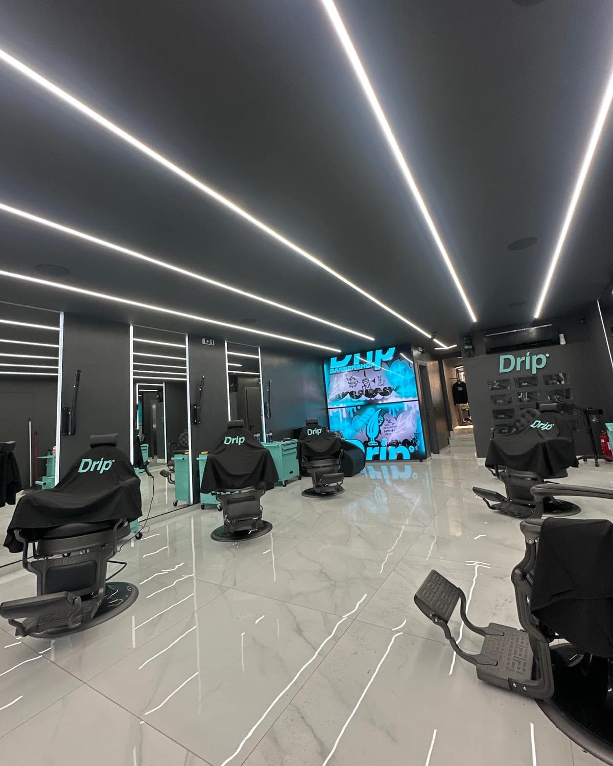Το Drip Barbershop στην Κηφισιά από μέσα: οι λευκές γραμμές φωτός στο ταβάνι, οι θέσεις και η οθόνη Drip στο βάθος